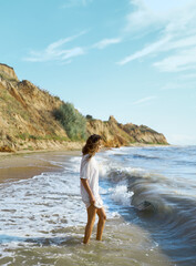 Charming summer beach woman enjoying sea waves along seashore with glifs on background. Concept people in nature. - obrazy, fototapety, plakaty