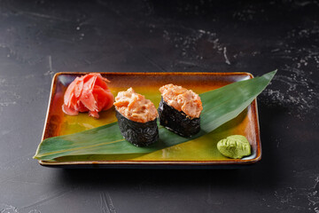 Gunkans with salmon on a plate. Decorated with bamboo leaf wasabi and ginger on a dark background.