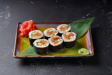 Vegetarian sushi roll on a rectangular plate on a dark background. Decorated with wasabi bamboo leaf and ginger.
