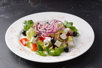 Greek salad on a white plate on a dark background.