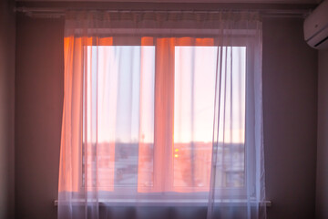 The rays of the morning sun fall through the white tulle on the window in the apartment. Sunrise, new day, atmospheric mood