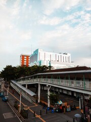 A large building under a beautiful blue sky, there is a bridge to ride a bus under it, and many people are active,