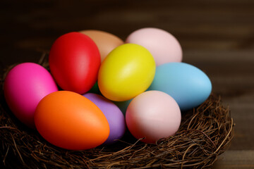Multi colored easter eggs in birds nest on dark wooden planks table closeup view selective focus. Easter celebration. Easter holiday banner, card, poster, voucher, invitation template