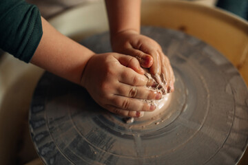 Child hands make earthenware cup on pottery wheel.