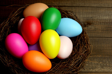 Multi colored easter eggs in birds nest on dark wooden planks table top closeup view selective focus. Easter holiday banner, card, poster, voucher, invitation template