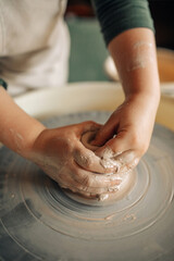 Child hands make earthenware cup on pottery wheel.