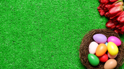 Multi colored easter eggs in birds nest and bouquet of red tulip flowers on green grass lawn background top view with copy space. Easter holiday banner, card, poster, voucher, header template