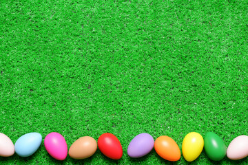 Frame from several multi colored easter eggs on green grass lawn background top view with copy space. Easter holiday banner, card, poster, voucher, invitation template