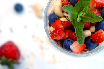 Healthy breakfast of strawberry parfait made with fresh fruit, yogurt, blueberries, flax seeds and muesli, white background. Close-up, top view.