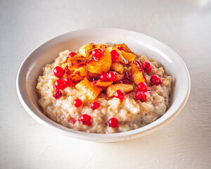 Oatmeal with caramelized apples and red currants in a white deep plate