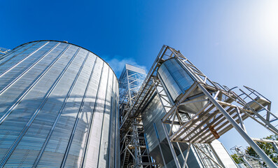 Fototapeta premium Grain elevators for crop storage. Metal bridge from the roof of metal tank. View from below. Closeup.