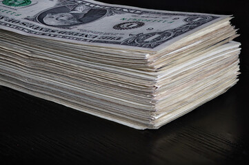 Stack of one dollar bills on a black wooden background.