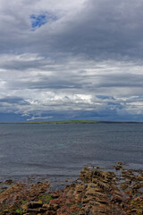 Looking across to the the island of Stroma, part of the Orkneys from the rocky beach at John O'Groats with dark rain clouds on the horizon.