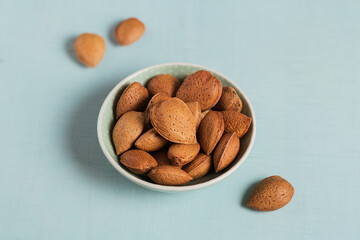 Pile of Almond nuts in a bowl on a light blue background