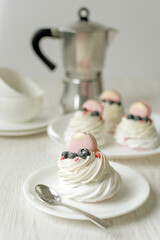Still life Pavlova meringue cake decorated macaron on white background. Tea cups and coffemaker on wood table