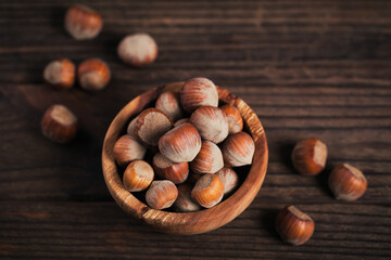 Pile of hazelnuts filbert in a wooden bowl on a dark wooden background
