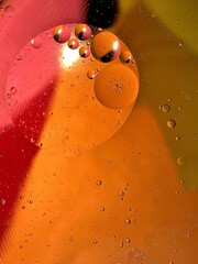 floating oil drops shimmering in different colors and shapes next to air bubbles on a colored background 
