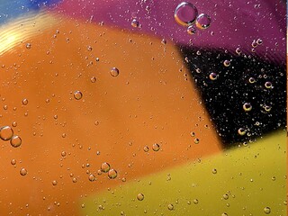 floating oil drops shimmering in different colors and shapes next to air bubbles on a colored background 