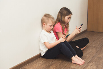 Two kids sitting at home and playing with smartphone. Children  technology, communication and internet concept.