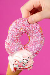 ice cream cone with a bitten donut with icing sprinkles on a pink background