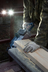 Hands of a joiner with a grinder machine. Flying shavings, wooden board. The work of a professional. Woodwork.