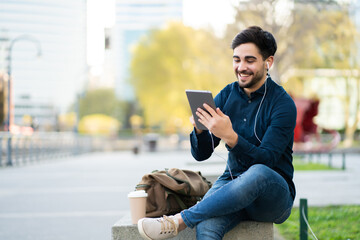 Fototapeta premium Young man having a video call on digital tablet outdoors.
