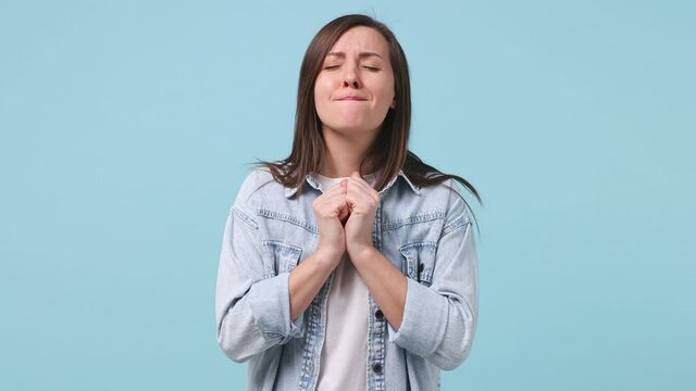Pleading long hair young woman 30s years old in denim jacket white t-shirt hold hands folded in prayer beg about something making wish keep fingers crossed isolated on pastel blue background studio