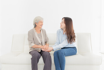 young Asian female holding hand of  old female in home, they feeling happy and smile, they sitting on sofa, mother's day, hand in hand, happiness family time