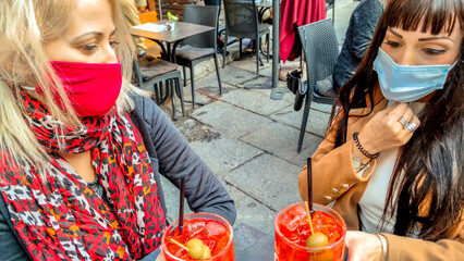 Women with surgical mask, toasting glasses of alcoholic drink cocktail in open pub. Festivity celebration in Coronavirus pandemic with safety social distancing for COVID-19 epidemic. happy hour time.