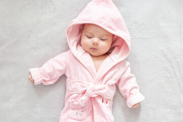 Baby girl in a Terry robe and diaper after bathing. Kid in a hood. Cute happy laughing baby girl in pink soft robe after bath. Baby in a clean and dry towel.