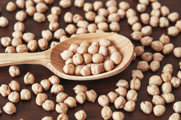 Raw chickpeas in a wooden spoon scattered on a wooden background. Top view. Copy, empty space for text