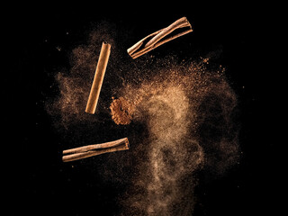 Cinnamon powder and sticks explosion on black background