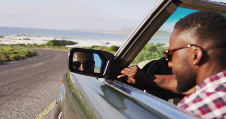 African american man adjusting side rear view mirror while sitting in convertible car - Powered by Adobe
