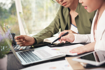 Side view of businesswoman's hands using laptop computer placed on messy office desktop. teamwork with business people analysis cost graph on desk at meeting room.