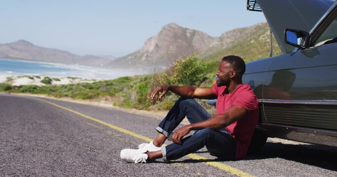African american man sitting near his broken down car on road