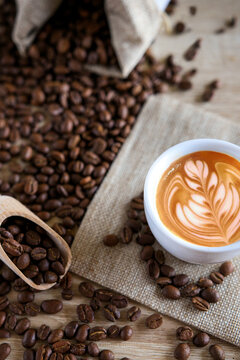 Bodeg&oacute;n de caf&eacute;. Fotograf&iacute;a compuesta de una taza de caf&eacute; con dibujos y granos de caf&eacute; alrededor dentro y fuera del saco. Concepto de sabor y cultura