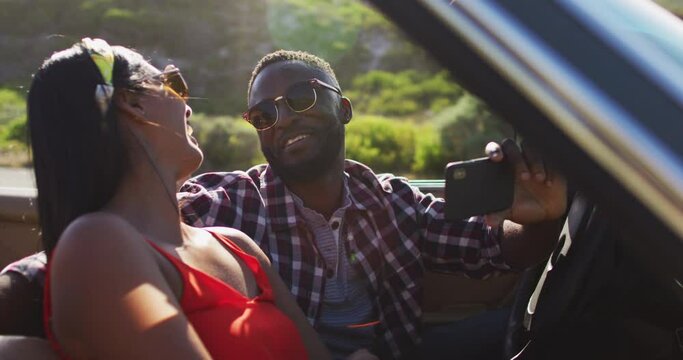 African american couple using smartphone while sitting in the convertible car on road