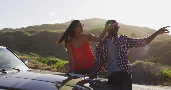 African american couple using maps for directions while standing near convertible car on road