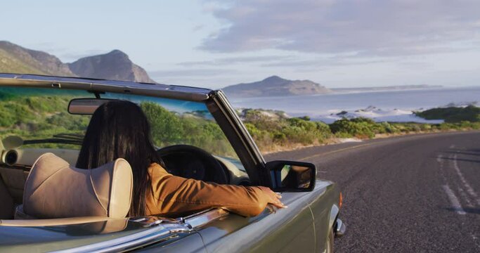 African american woman driving along country road in convertible car