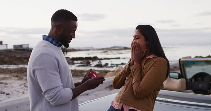 African american man proposing his girlfriend with a ring near the convertible car on the road