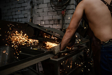 Muscular blacksmith in a leather apron sawing metal in a forge, glowing sparks fly in different directions