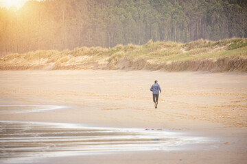 Fototapeta na wymiar Corredor entrena corriendo por la playa de buena mañana en un día soleado frente al mar.