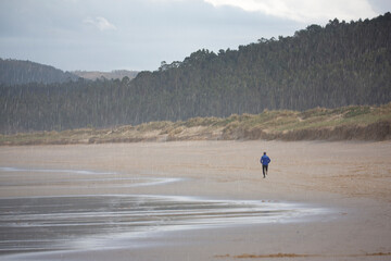 Corredor entrena corriendo por la playa de buena mañana en un día soleado frente al mar.