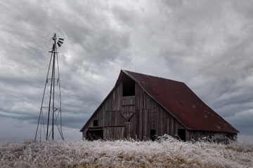 An old barn next to a broken windmill on a stormy, icey, dramatic day © Cavan