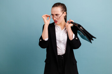 Indignant girl standing in a black suit holding a briefcase over her shoulder standing with a serious face. Business girl.