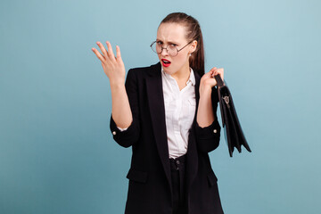 Indignant girl standing in a black suit holding a briefcase over her shoulder