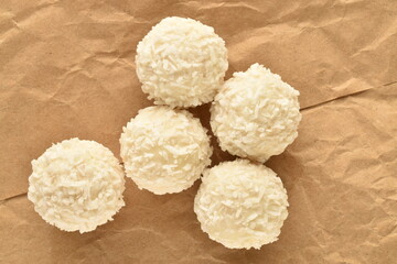 Several delicious sweets with coconut flakes on brown paper, close-up, top view.