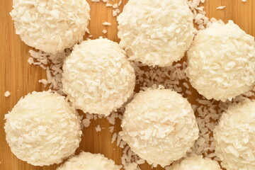 Three delicious sweets with coconut on a bamboo plate, close-up, top view.