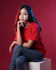 Young female model wearing blank T-shirt in studio background. Woman in cheerful pose with blue and red lighting. Modern shirt mockup. Young women are stylish like adult models. Pretty sheer makeup.