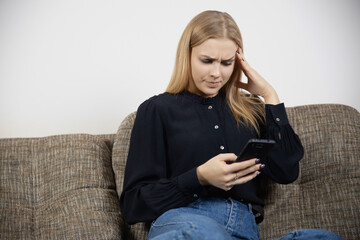 Stressed thoughtful young caucasian female with phone received bad news in message sitting on couch